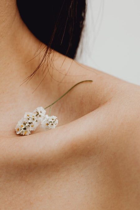 Naakte schouder van een dame met in het sleutelbeen een klein delicaat bloempje.